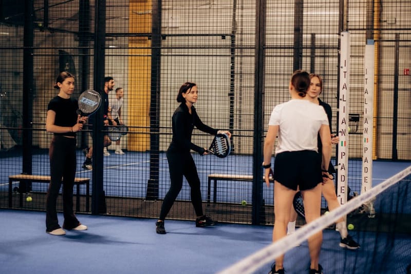 Padel player swinging a carbon racket on an indoor court mid-rally